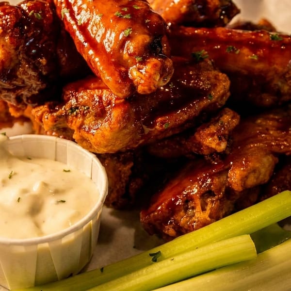 A close-up of glazed chicken wings with a side of ranch dressing and celery sticks.