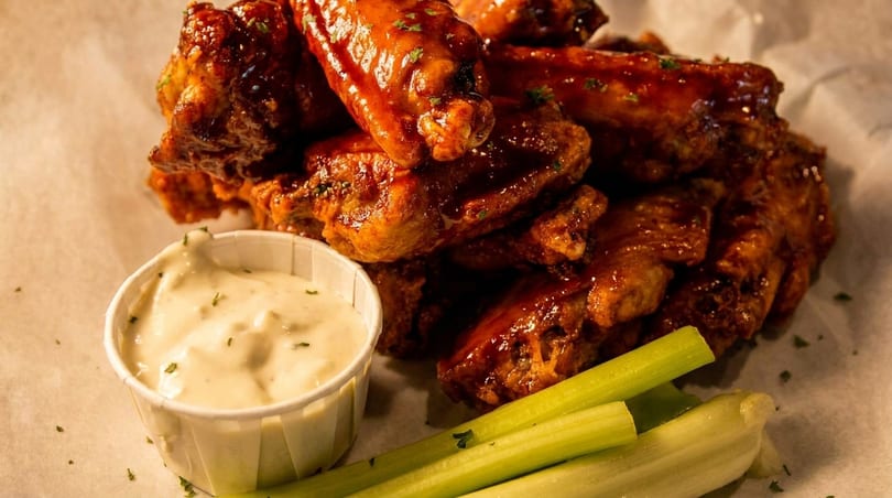 A close-up of glazed chicken wings with a side of ranch dressing and celery sticks.