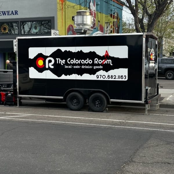 Black "The Colorado Room" food truck with white logo and phone number parked on a city street.