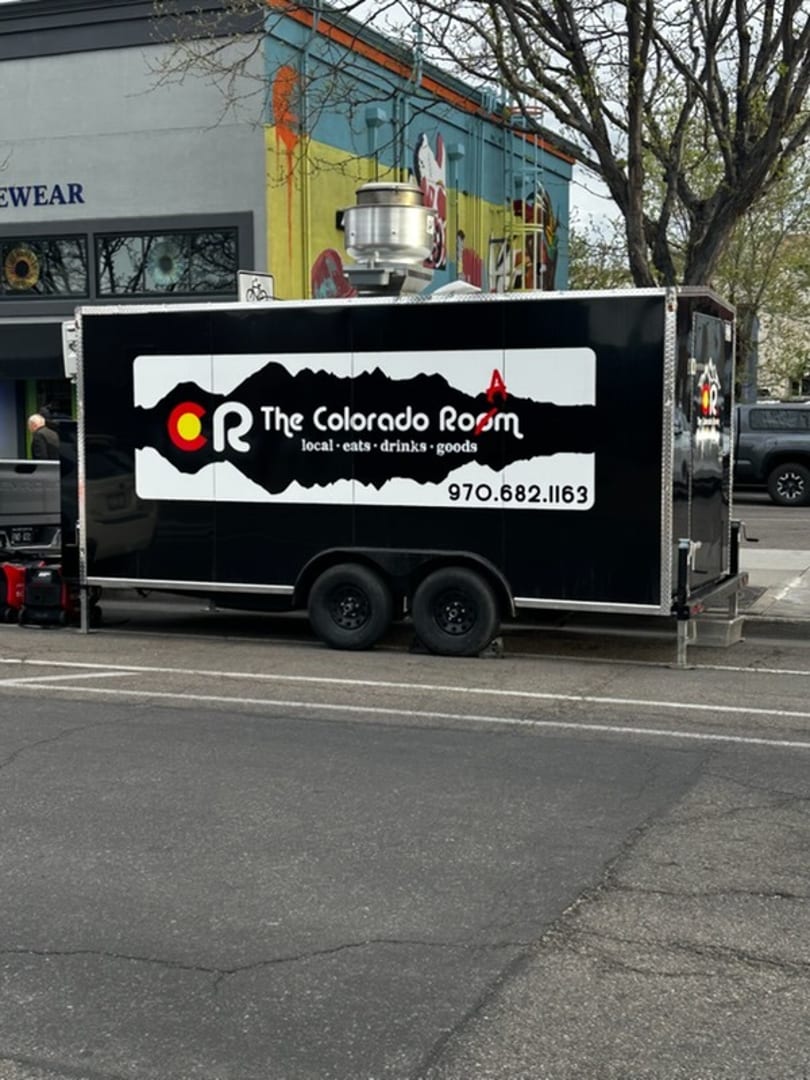 Black "The Colorado Room" food truck with white logo and phone number parked on a city street.