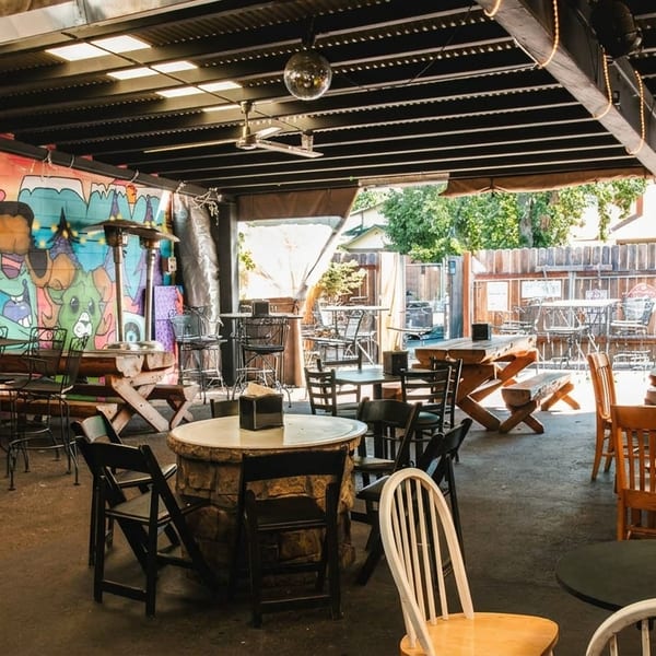 An outdoor patio with diverse seating, colorful graffiti, and a disco ball under a covered roof.