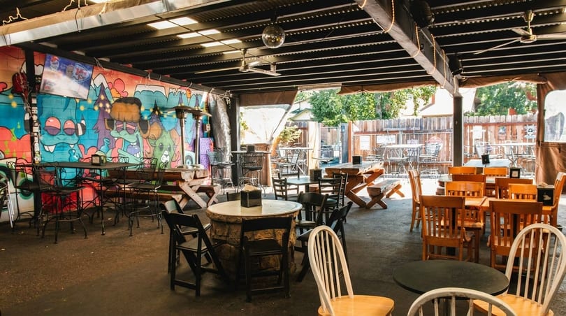 An outdoor patio with diverse seating, colorful graffiti, and a disco ball under a covered roof.