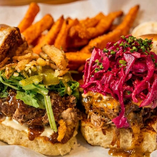 Two gourmet sliders with various toppings and a side of sweet potato fries.
