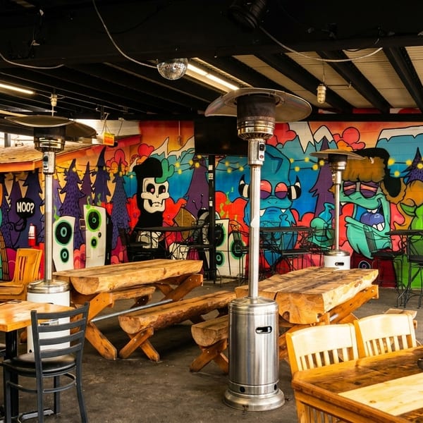 Outdoor patio with wooden tables, black chairs, and a colorful graffiti mural on the back wall.