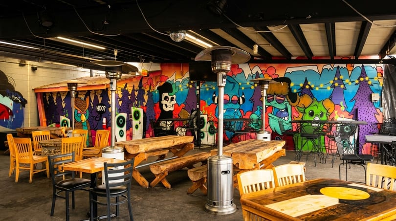 Outdoor patio with wooden tables, black chairs, and a colorful graffiti mural on the back wall.