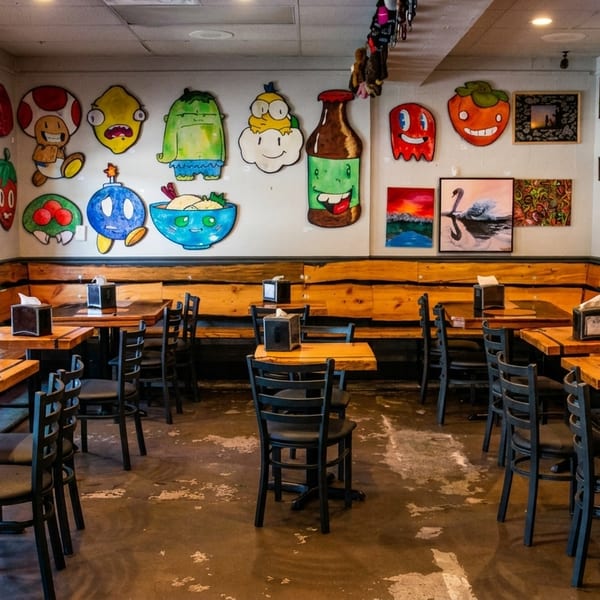 Restaurant interior with wooden tables, black chairs, and walls adorned with colorful, whimsical cartoon art.