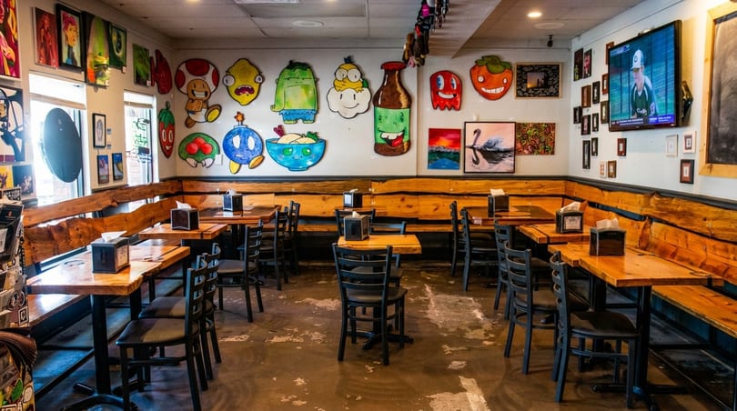 Restaurant interior with wooden tables, black chairs, and walls adorned with colorful, whimsical cartoon art.