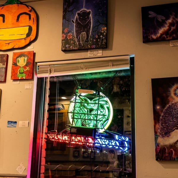 A wall filled with diverse artwork, including a large pumpkin, character portraits, and a neon sign.