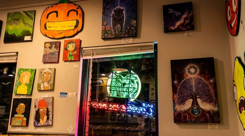A wall filled with diverse artwork, including a large pumpkin, character portraits, and a neon sign.