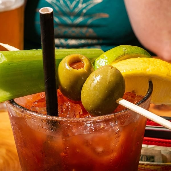 Close-up of a Bloody Mary cocktail garnished with celery, olives, and lemon on a wooden table.