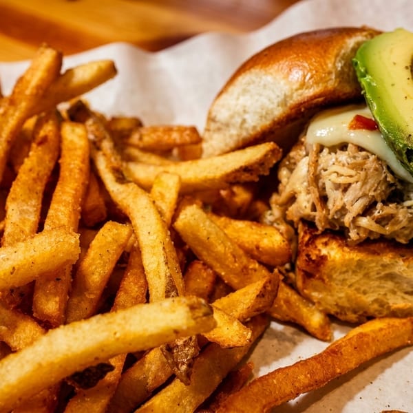 Pulled pork sandwich with avocado and melted cheese, served with a side of golden french fries.