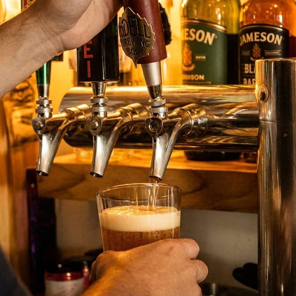 Bartender pouring a beer from a tap into a glass, with liquor bottles in the background.