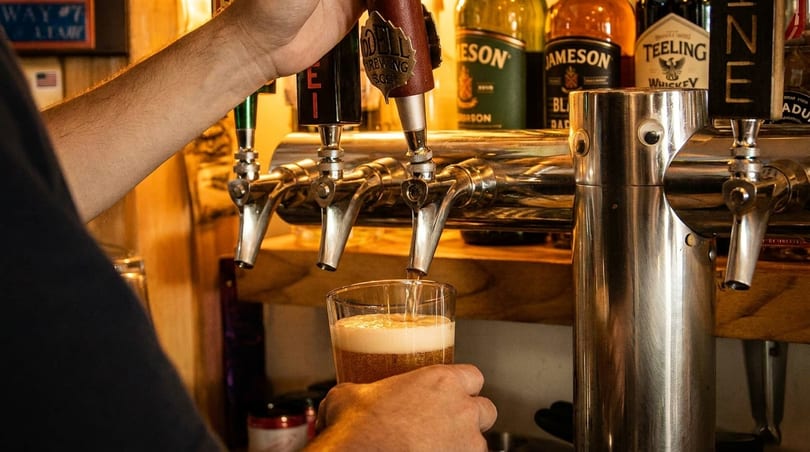 Bartender pouring a beer from a tap into a glass, with liquor bottles in the background.